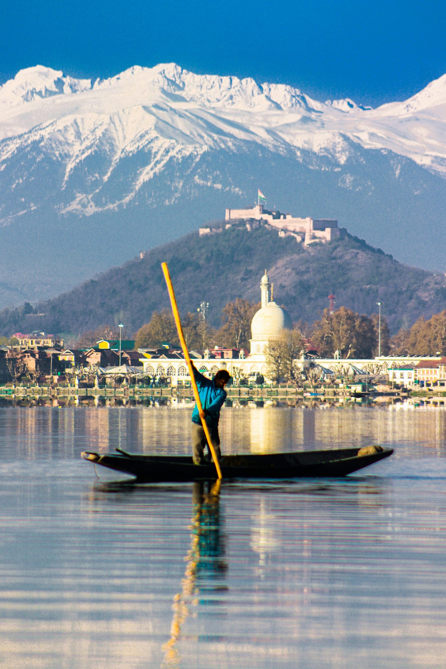 A lone man paddles a boat on Dal Lake against the backdrop of snowcapped mountains, showcasing serene beauty.