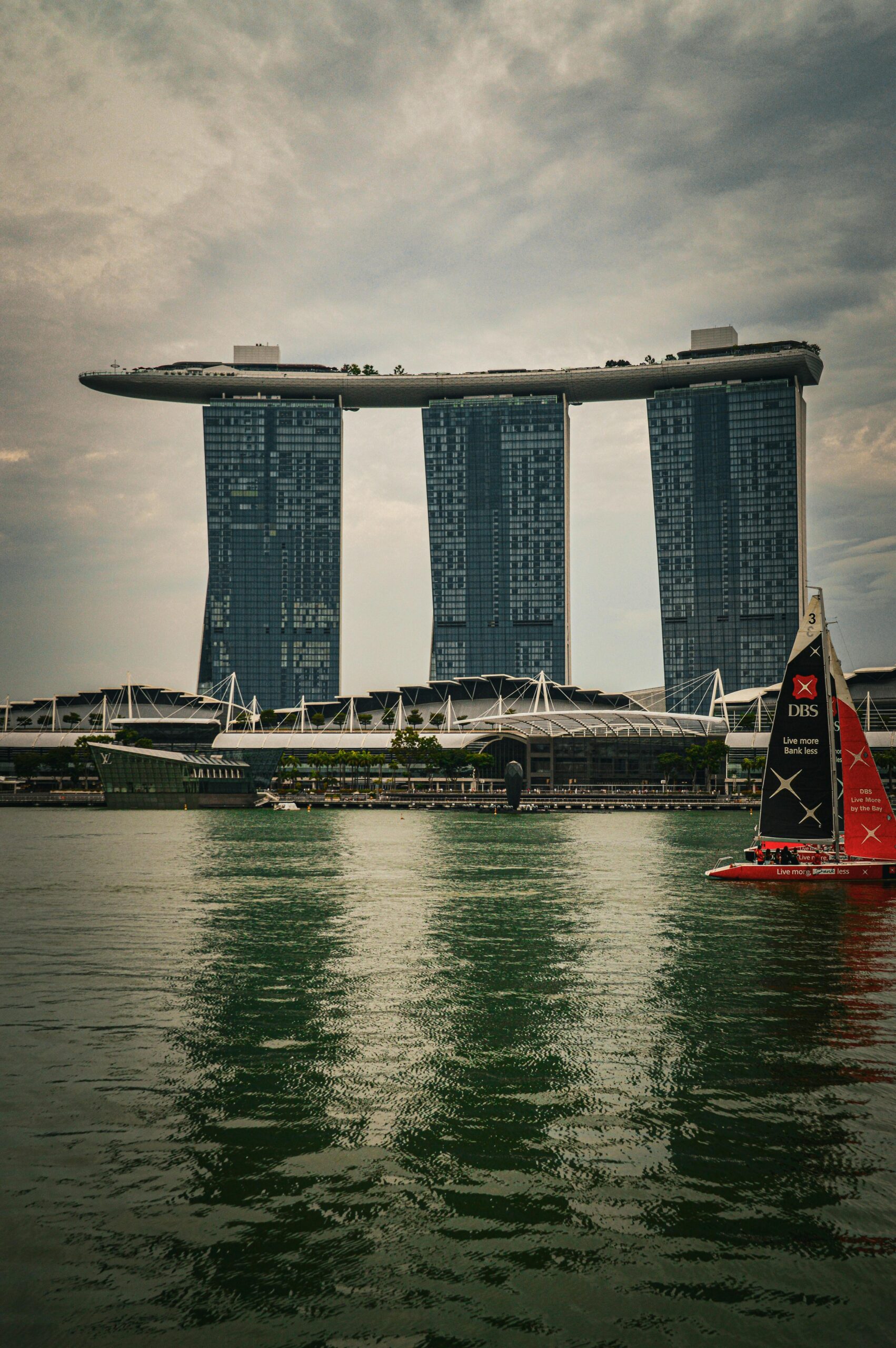 View of Marina Bay Sands with a sailboat on the water in Singapore.